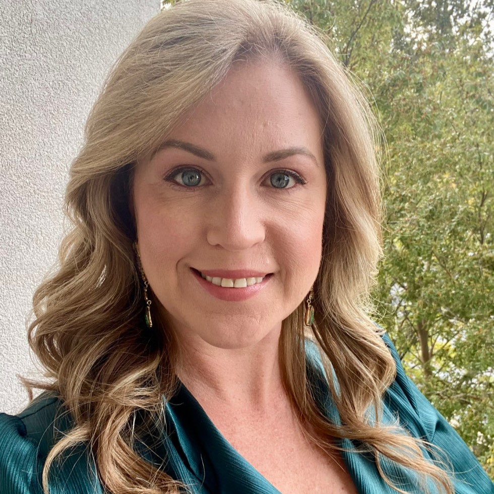 Erin Bendily headshot. She has a blue shirt and trees are in the background. 