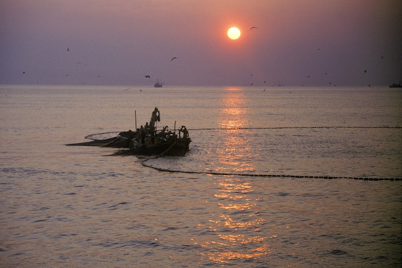 a fishing boat with it's net in the water at sunset